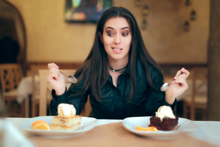 Girl Trying to Decide Between Vanilla and Chocolate wedding Cake Dessert. Cute woman at the restaurant choosing what to eat between two plates