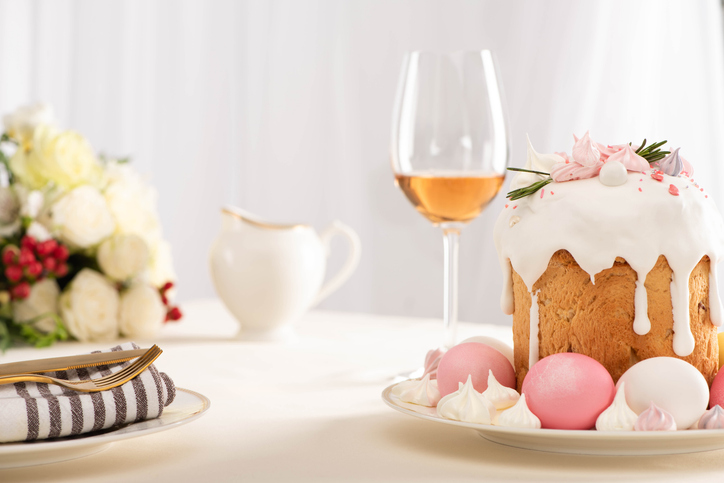 selective focus of delicious cake decorated with meringue with pink and white eggs on plate near wine glass and flowers