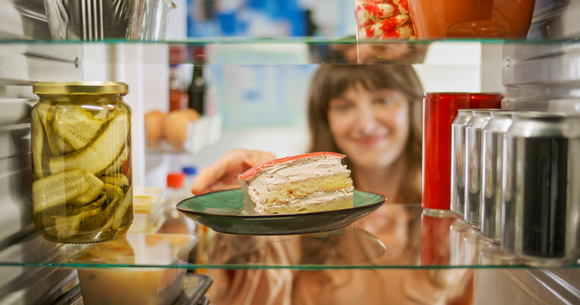 woman reaching into the fridge to grab a slice of cake
